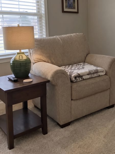 Lampe de table en céramique verte prévisualisée sur une table d'appoint près d'un fauteuil avec l'IA